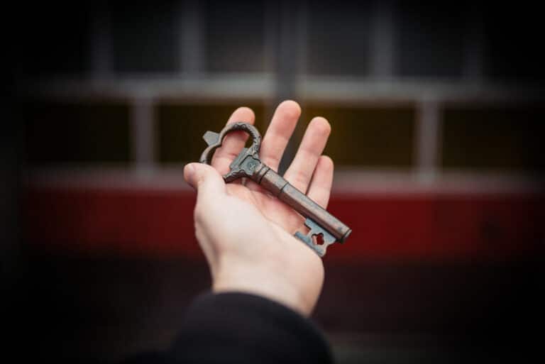 A hand holding an old key in front of a wooden door